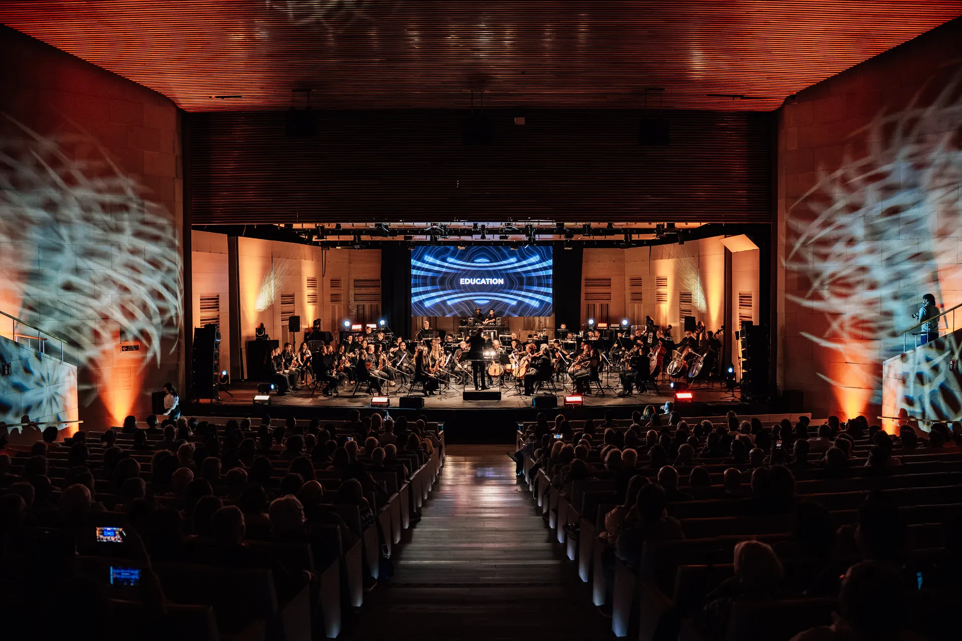 El espectáculo en un auditorio de madera, con la orquesta en escena y proyecciones en las paredes